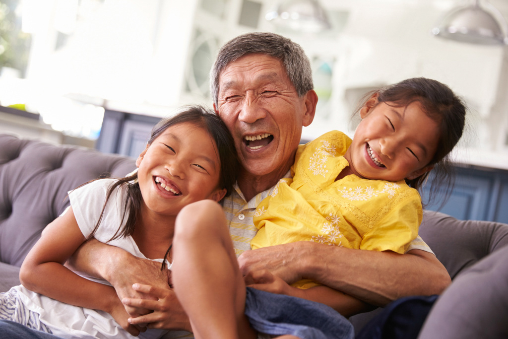 An older man and two young children sitting on a couch smiling in a warm embrace .
