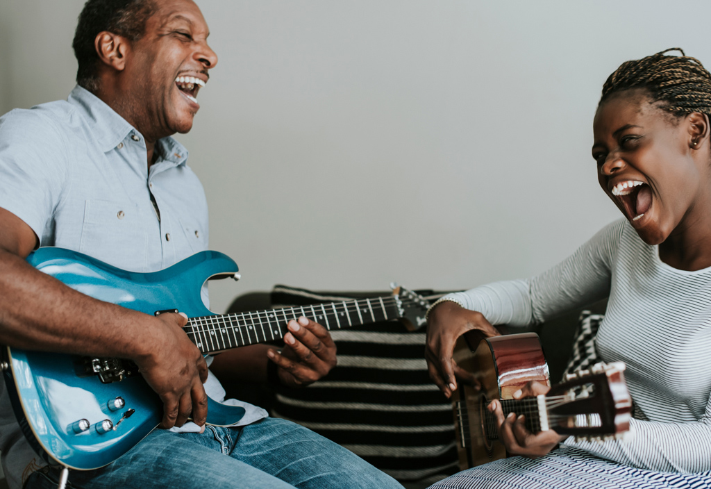 Man and teenage girl playing guitars facing one another, smiling. 