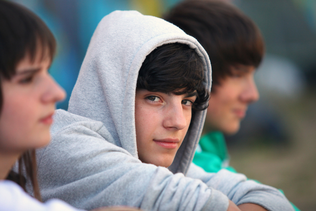 Somber male teenager wearing a hoodie looks at camera.