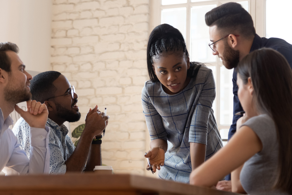 Female employee leaning over conference table while speaking to four coworkers.