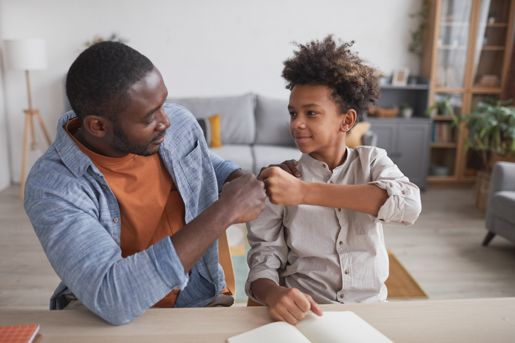 Male fist bumping with a male teenager while smiling.