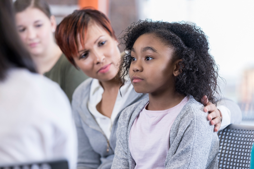 Woman puts arm around young girl sitting next to her.