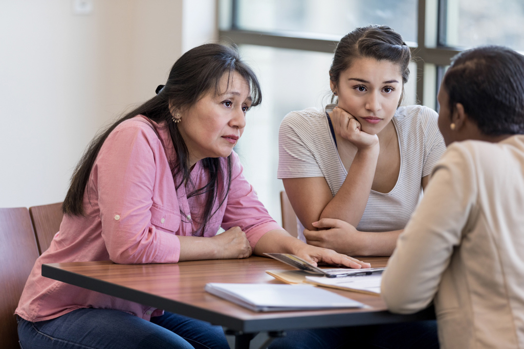 Woman and teenage girl sit across from another woman with serious expressions.