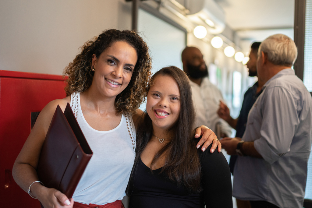 A woman with her arm around a teenage girl, smiling.