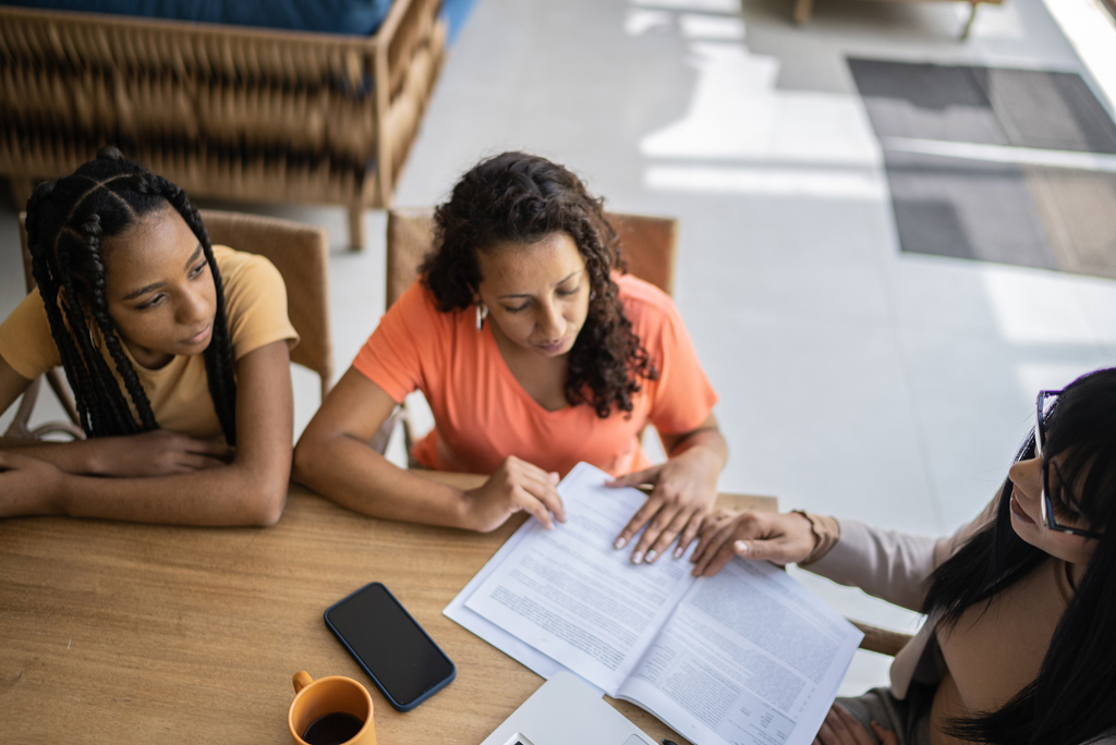 Woman and teenage girl sit across from another woman as they review paperwork.