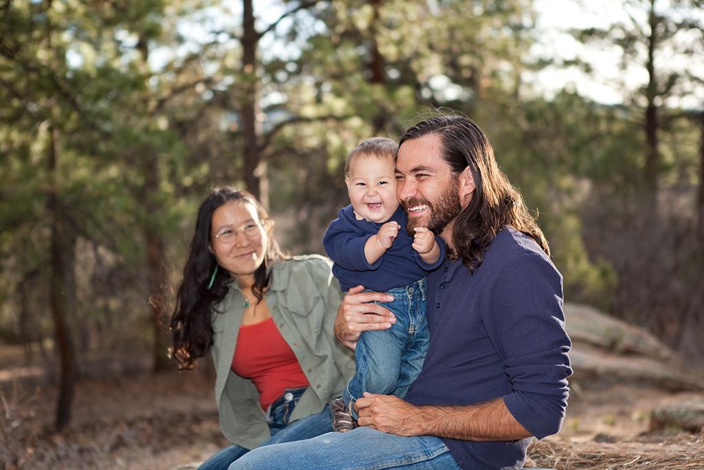 Man, woman, and child sitting in nature, smiling.