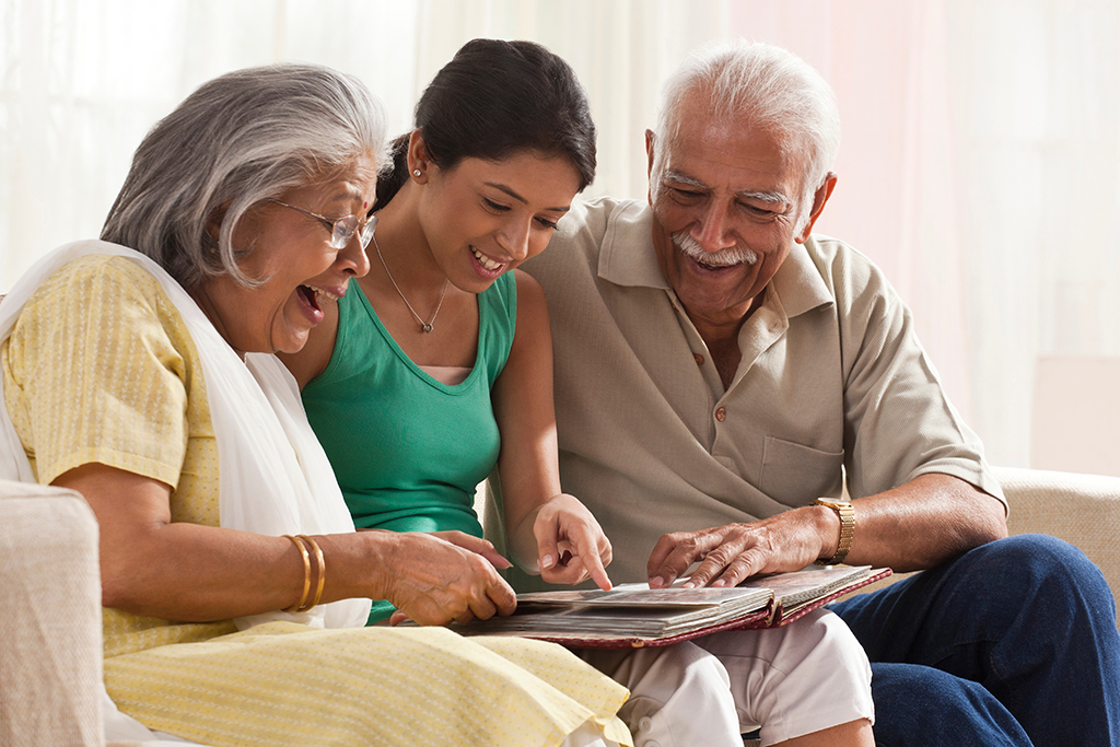 Teenage girl sitting between older man and woman on a couch looking at a photo album