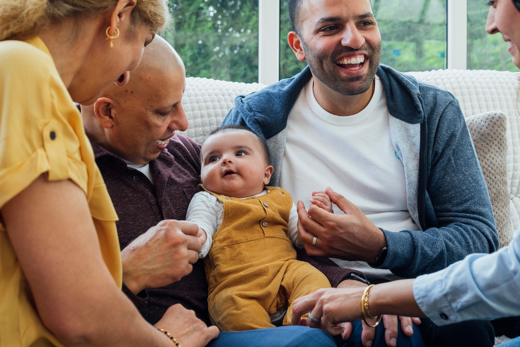 A group of people sitting closely on a couch, engaging with a baby.