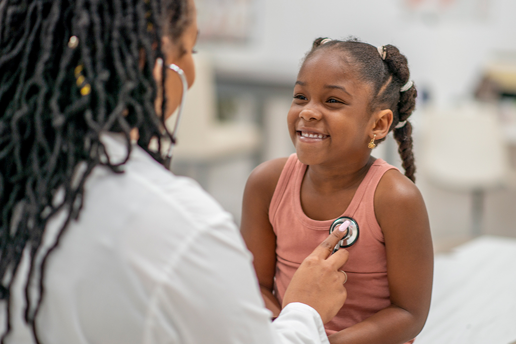 A healthcare professional is using a stethoscope to listen to the chest of a young girl sitting on an examination table