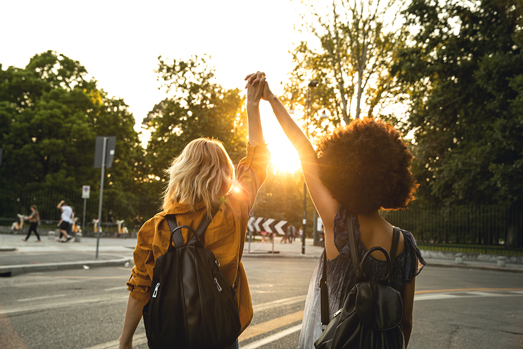 Two young women holding hands while walking together in the city at sunset.