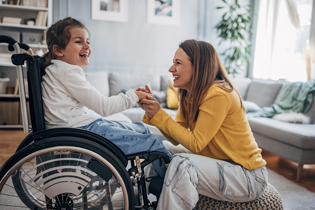 young female child in a wheelchair laughing holding hands with an adult female sitting in front of her