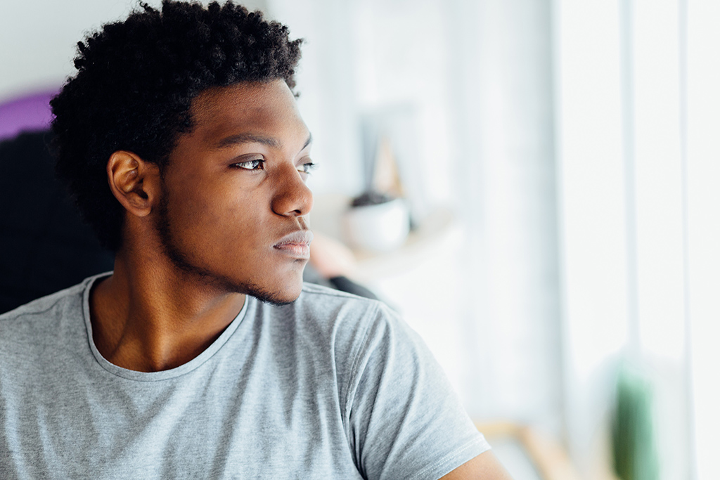 Headshot portrait of young man looking aside and appearing isolated in front of a blurred indoors background.
