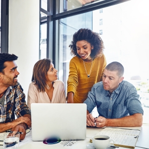 Diverse group of team members in office surrounding a laptop