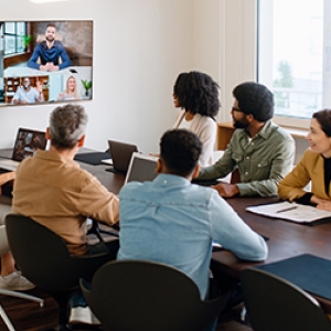 A group of child welfare professionals in a conference room engaged in a video conference call with their colleagues on-screen.