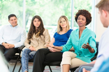 Multi-ethnic group sitting in circle listening to one person speak.