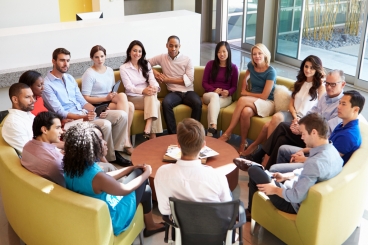 Multi-ethnic group of fifteen adults sitting in circle listening to one person speak.