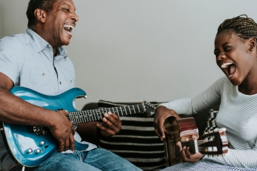 Man and teenage girl playing guitars facing one another, smiling.