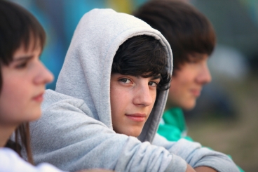 Somber male teenager wearing a hoodie looks at camera.