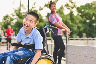 A young boy sitting in a wheelchair outside smiling.