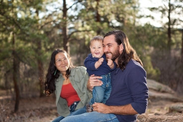 Man, woman, and child sitting in nature, smiling.