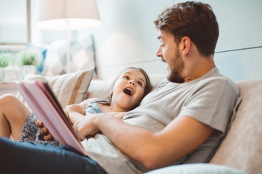 adult male and female child sitting on a couch reading a book