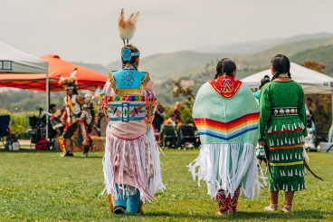Three women dressed in Tribal attire walking together with their backs facing the camera.