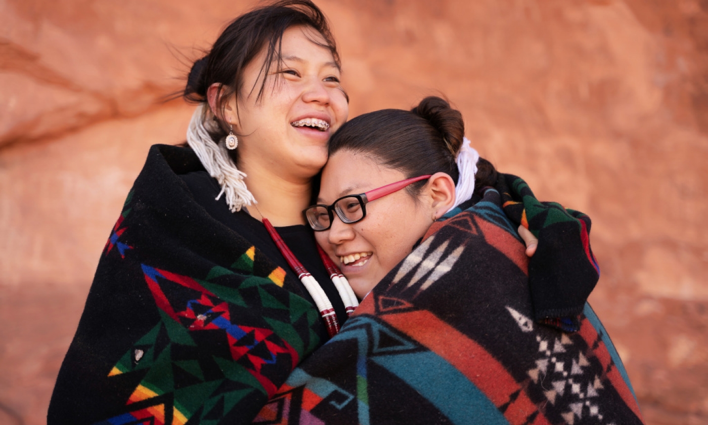 Two American Indian/Alaska Native women smiling while giving each other a hug.