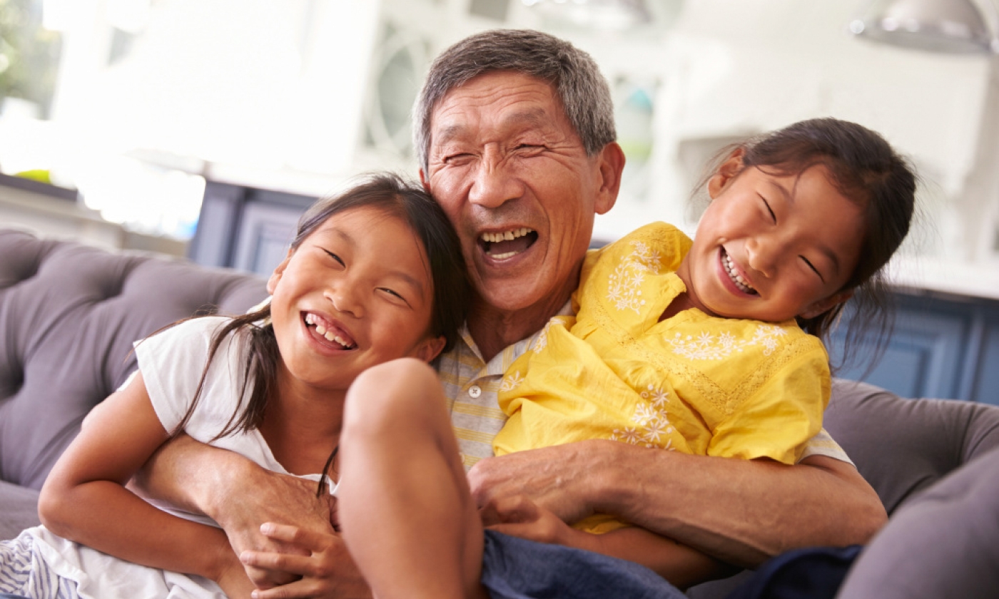 An older man and two young children sitting on a couch smiling in a warm embrace .