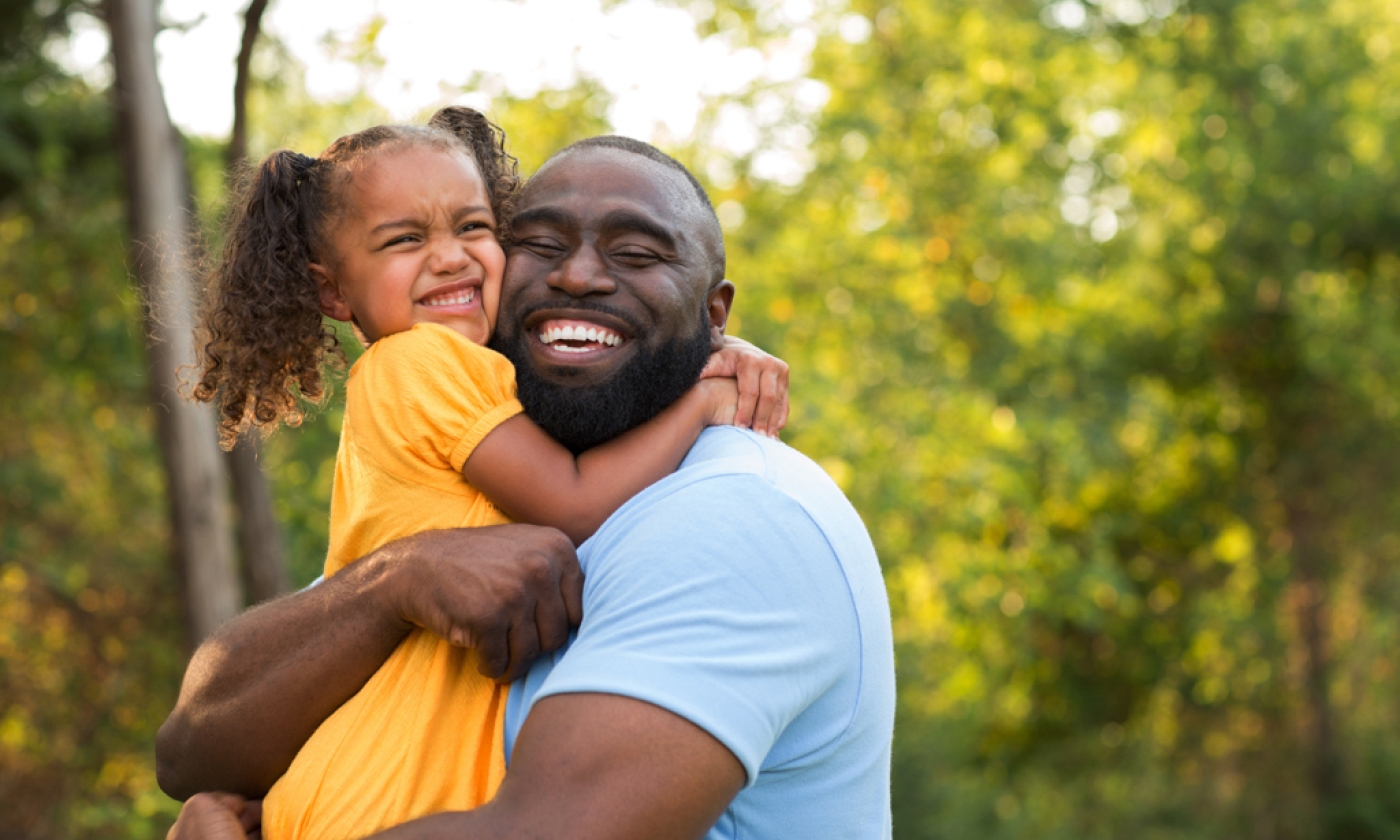 Black man hugging a young girl smiling.