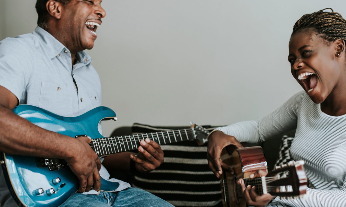 Man and teenage girl playing guitars facing one another, smiling.
