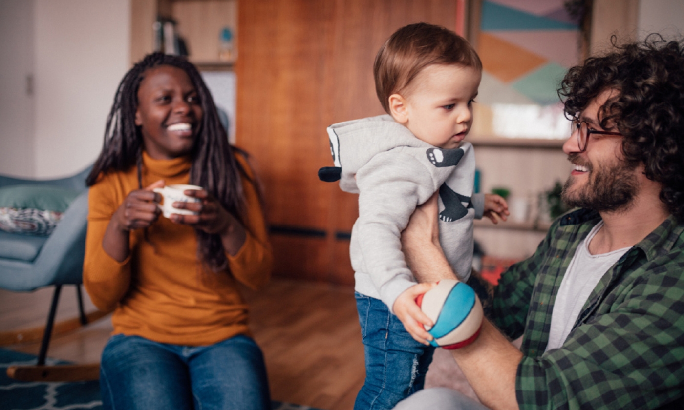 Man holding child with woman sitting next to them smiling.