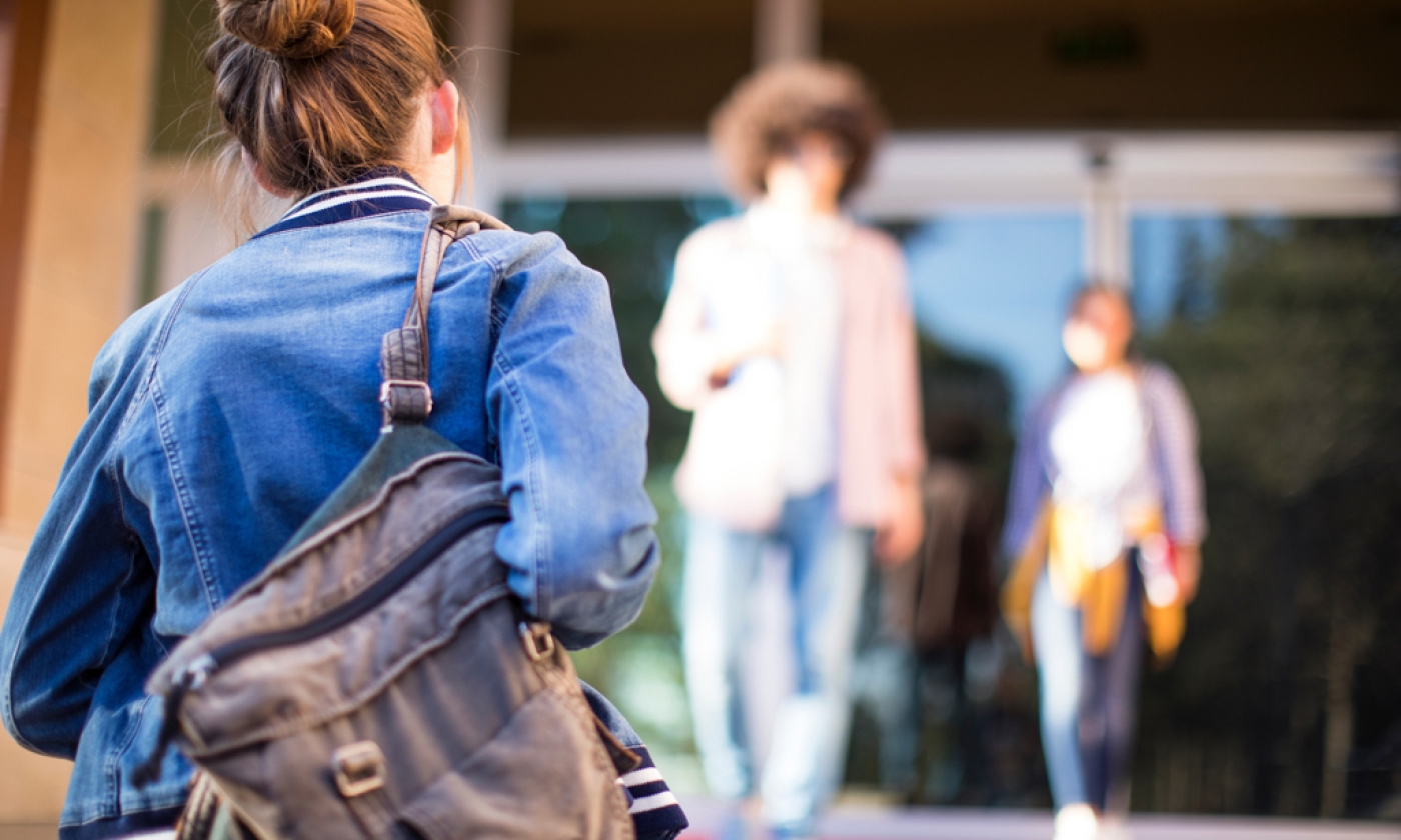 Woman wearing a backpack walking towards a building.