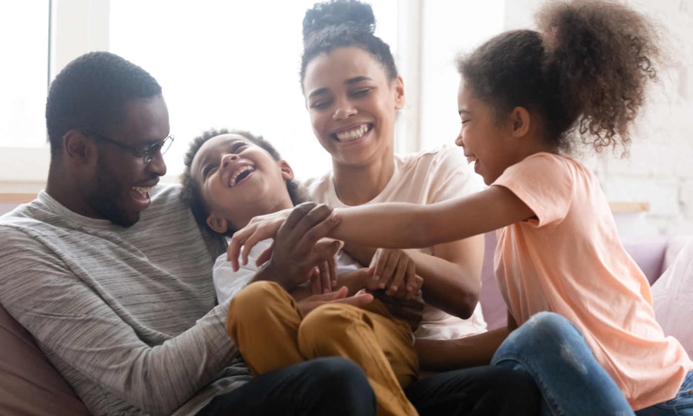 Adult male and female sitting on sofa with a young boy and girl, laughing.