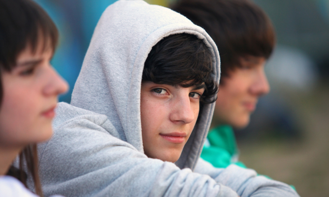 Somber male teenager wearing a hoodie looks at camera.