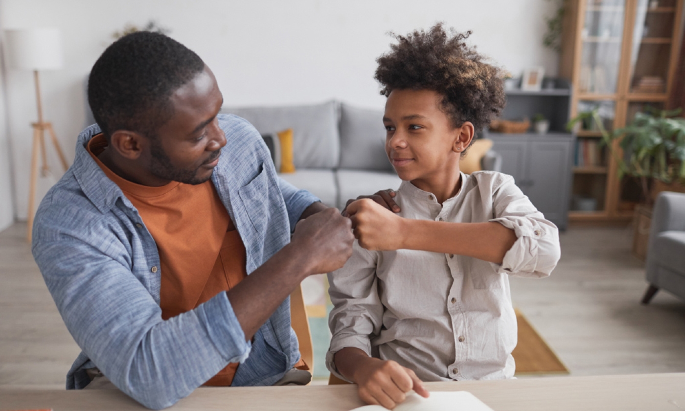 Male fist bumping with a male teenager while smiling.