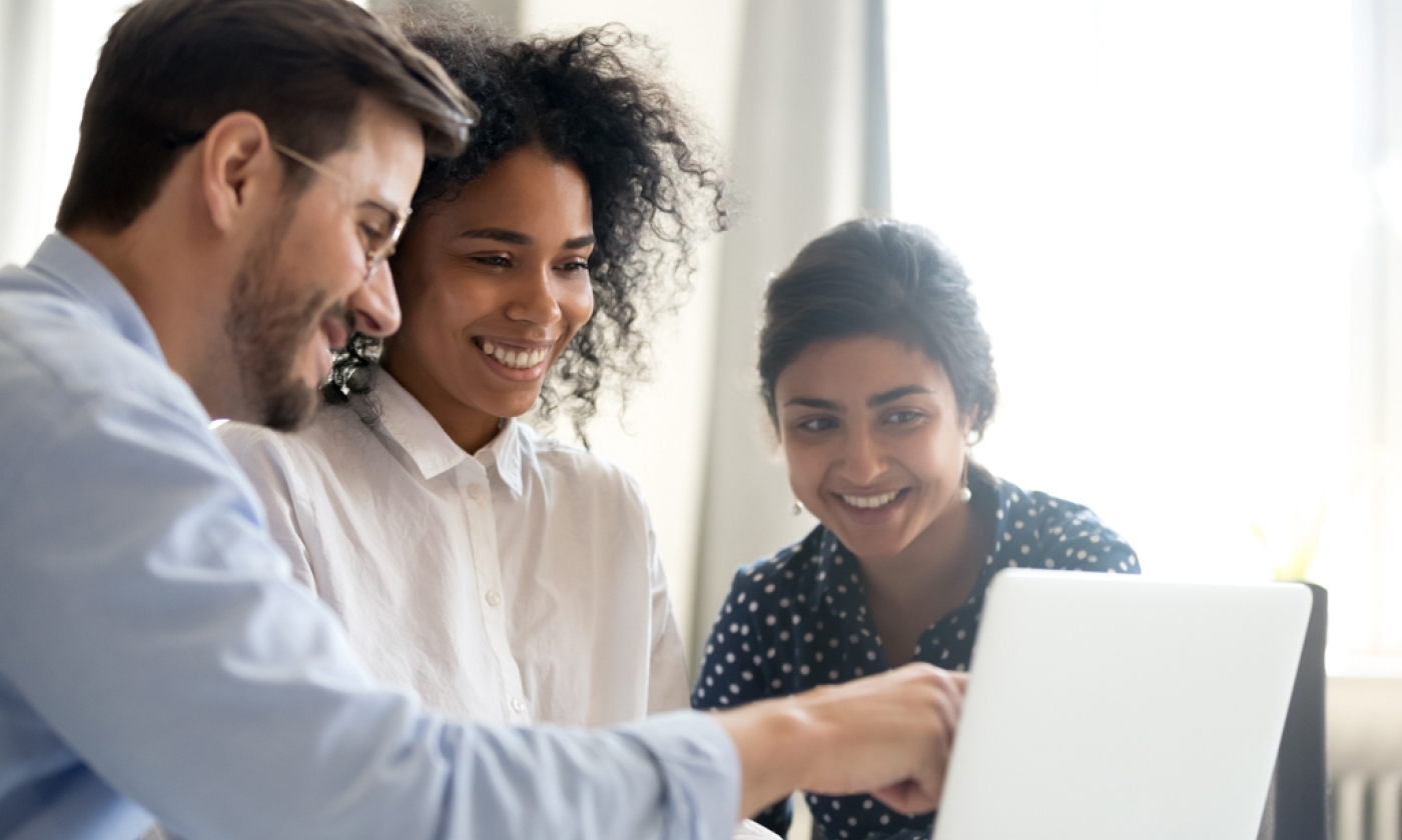 Two women and a male look at the laptop screen while the man points to the screen.