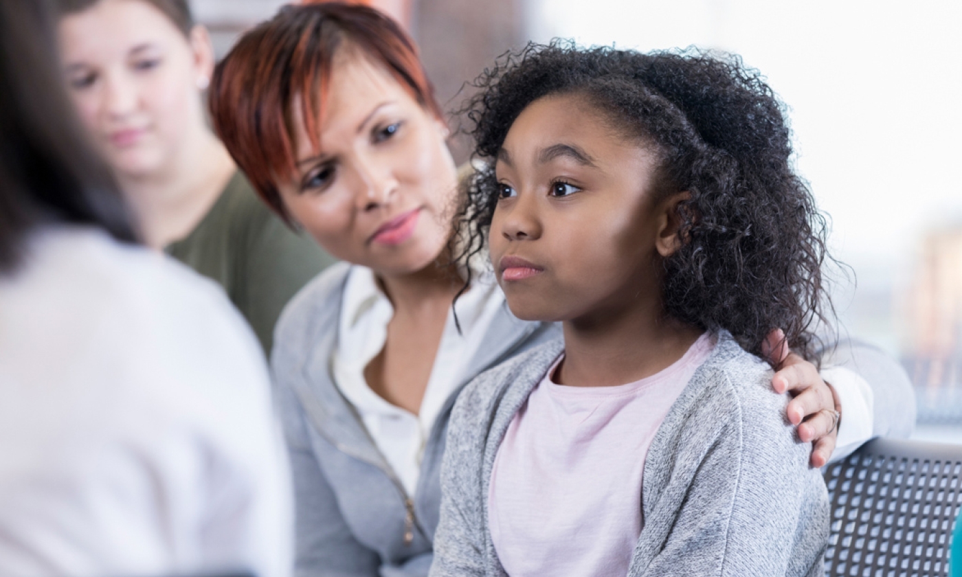 Woman puts arm around young girl sitting next to her.