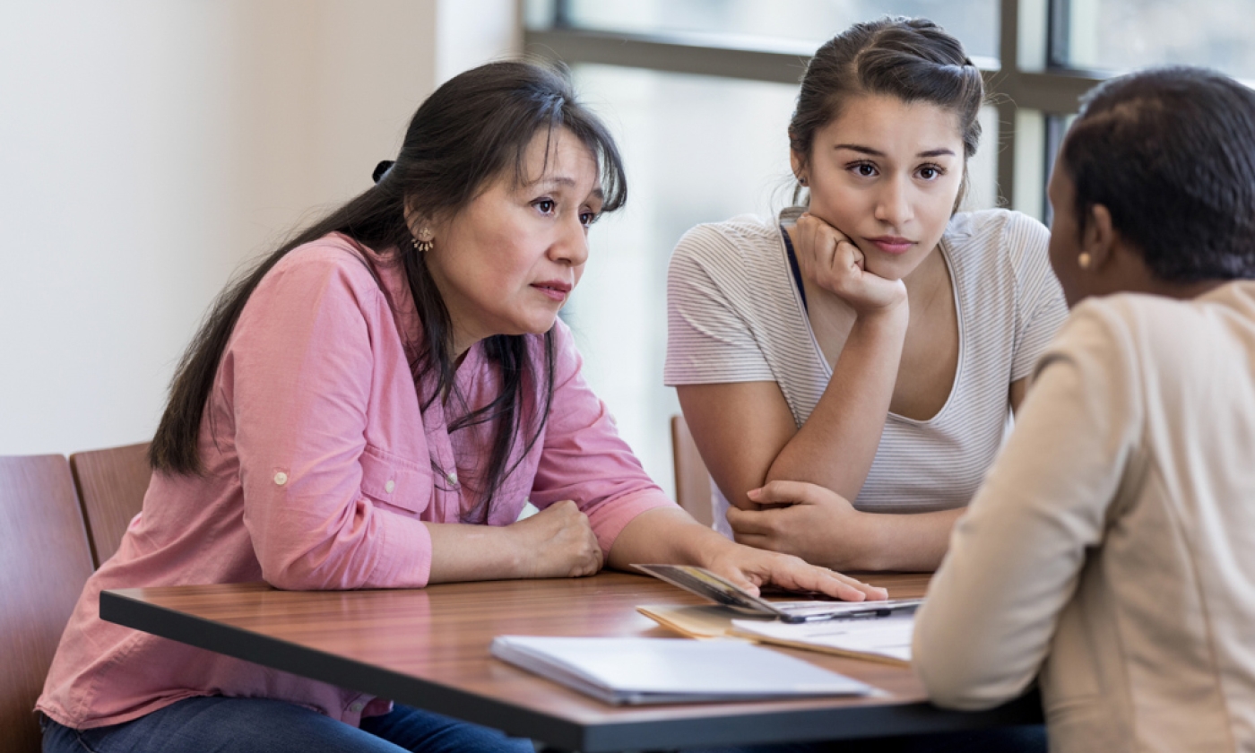 Woman and teenage girl sit across from another woman with serious expressions.