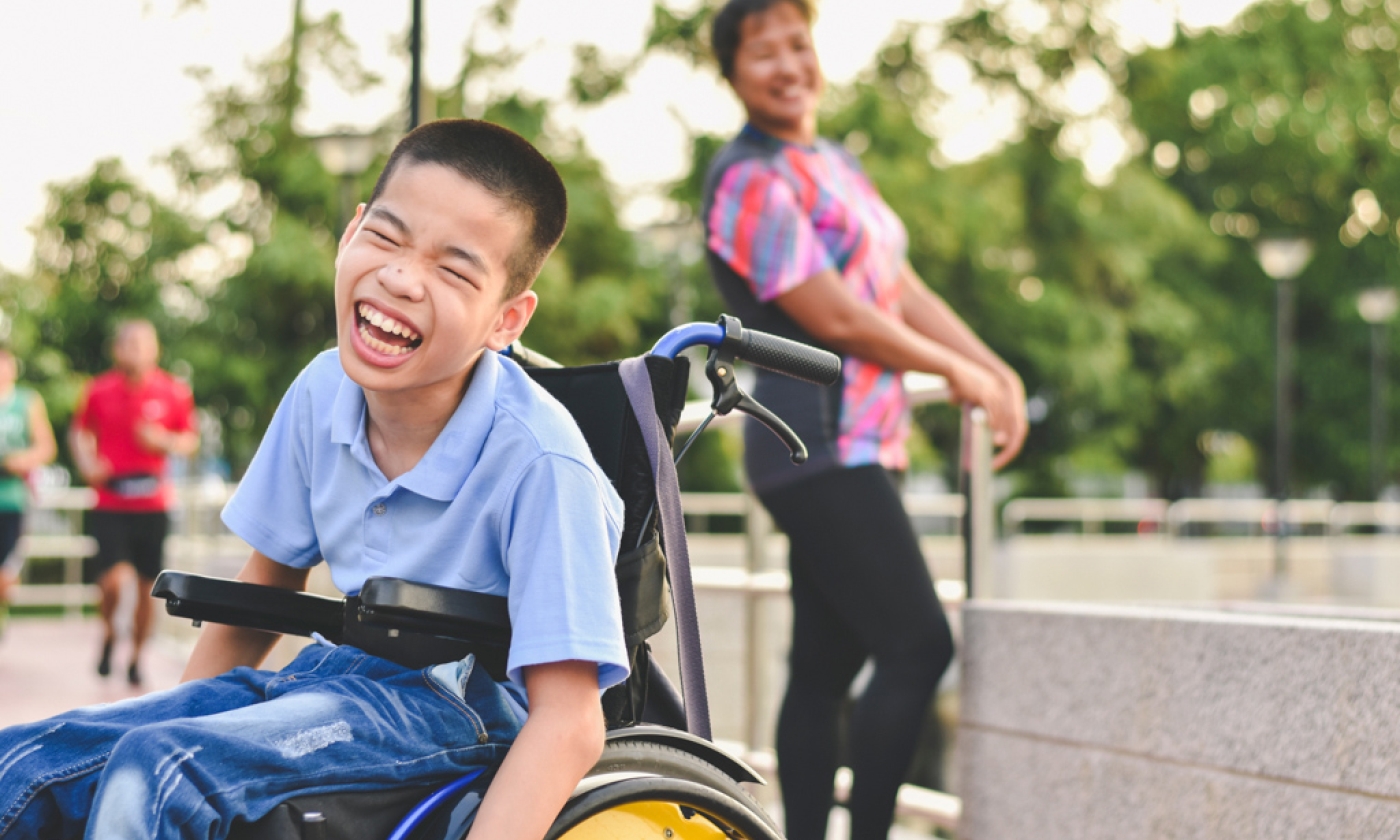 A young boy sitting in a wheelchair outside smiling.