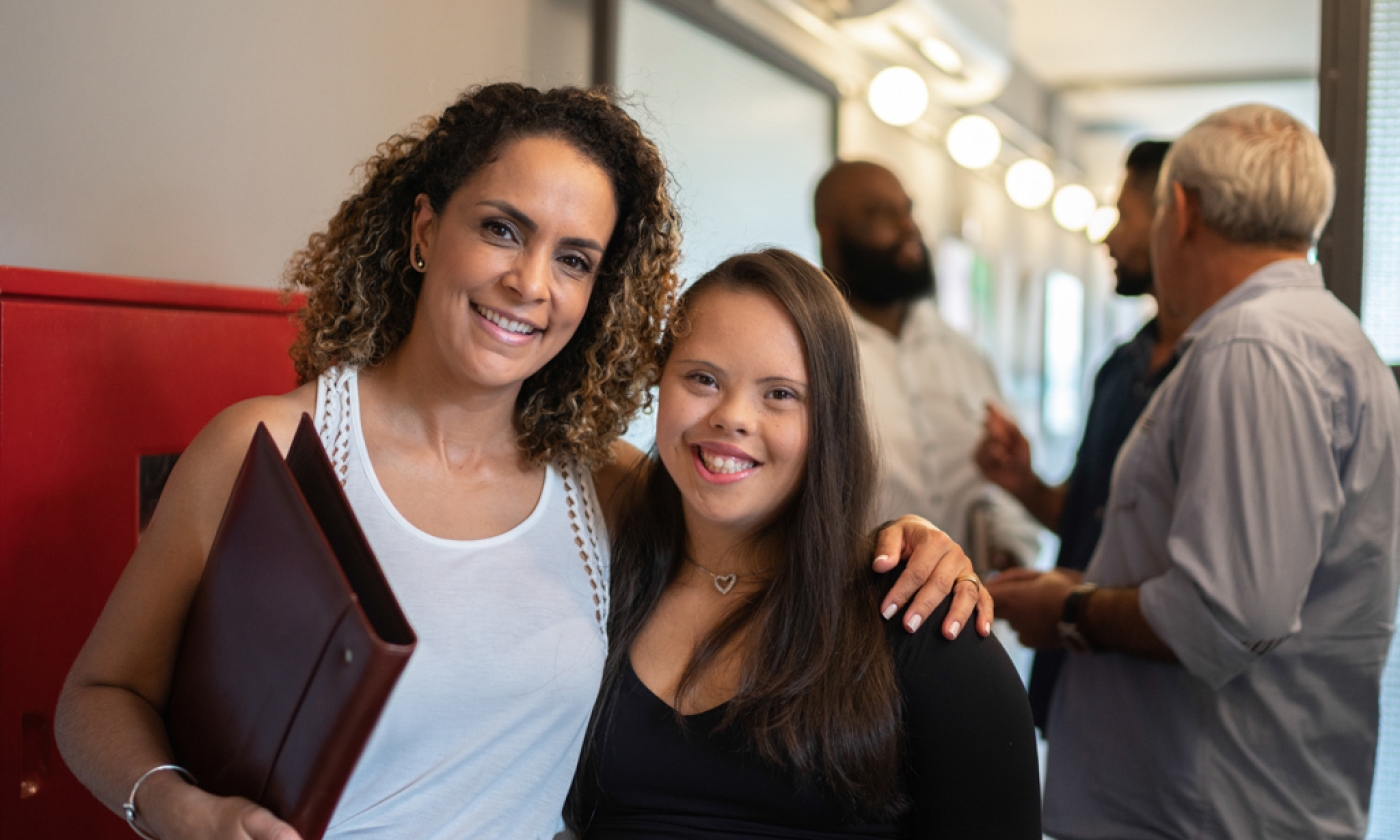A woman with her arm around a teenage girl, smiling.