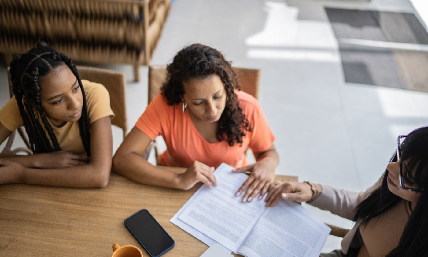 Woman and teenage girl sit across from another woman as they review paperwork.