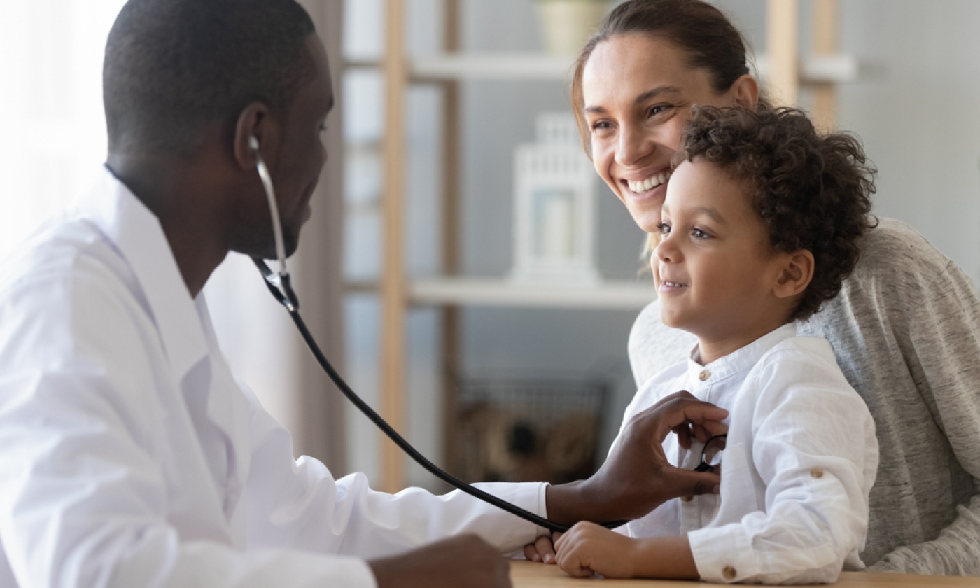 An adult male putting a stethoscope on a young child who is sitting in the lap of an adult woman.