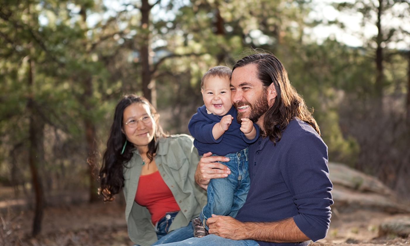 Man, woman, and child sitting in nature, smiling.