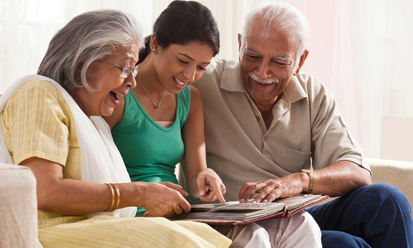 Teenage girl sitting between older man and woman on a couch looking at a photo album