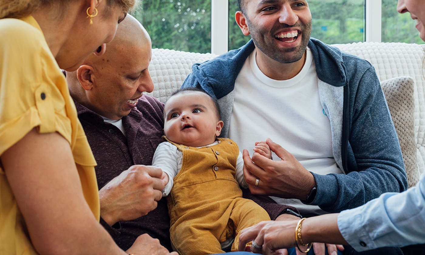 A group of people sitting closely on a couch, engaging with a baby.