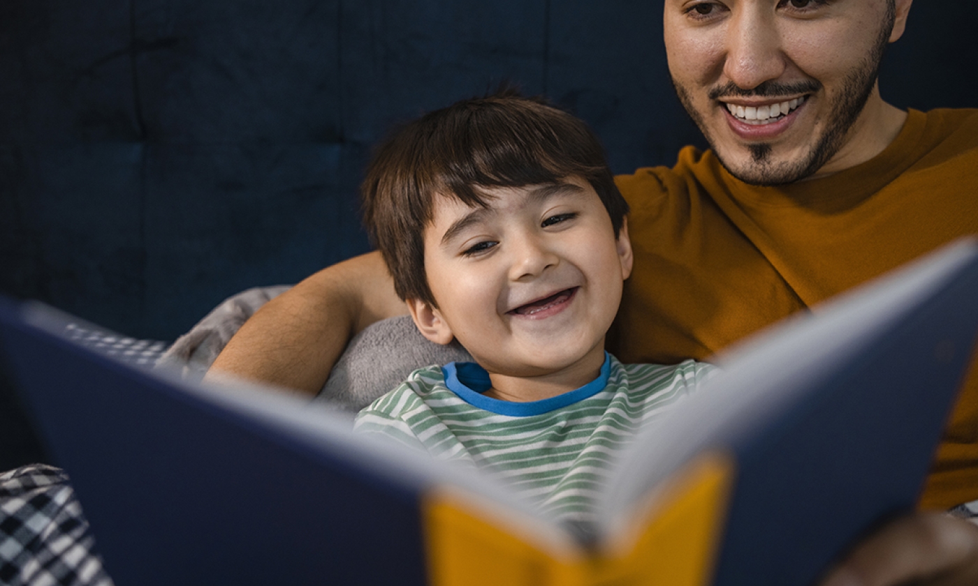 Man and young boy smiling as they look at a book they are holding.