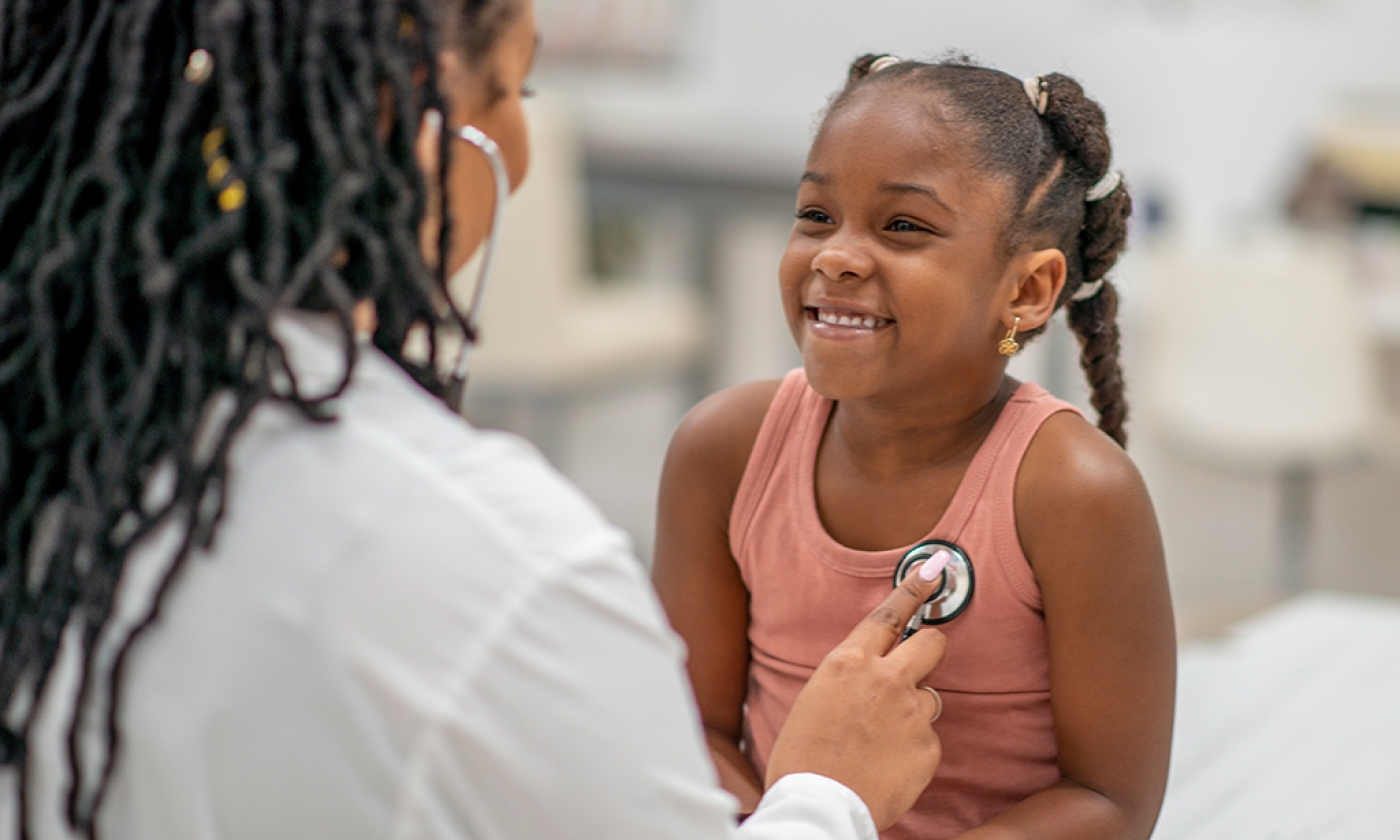 A healthcare professional is using a stethoscope to listen to the chest of a young girl sitting on an examination table