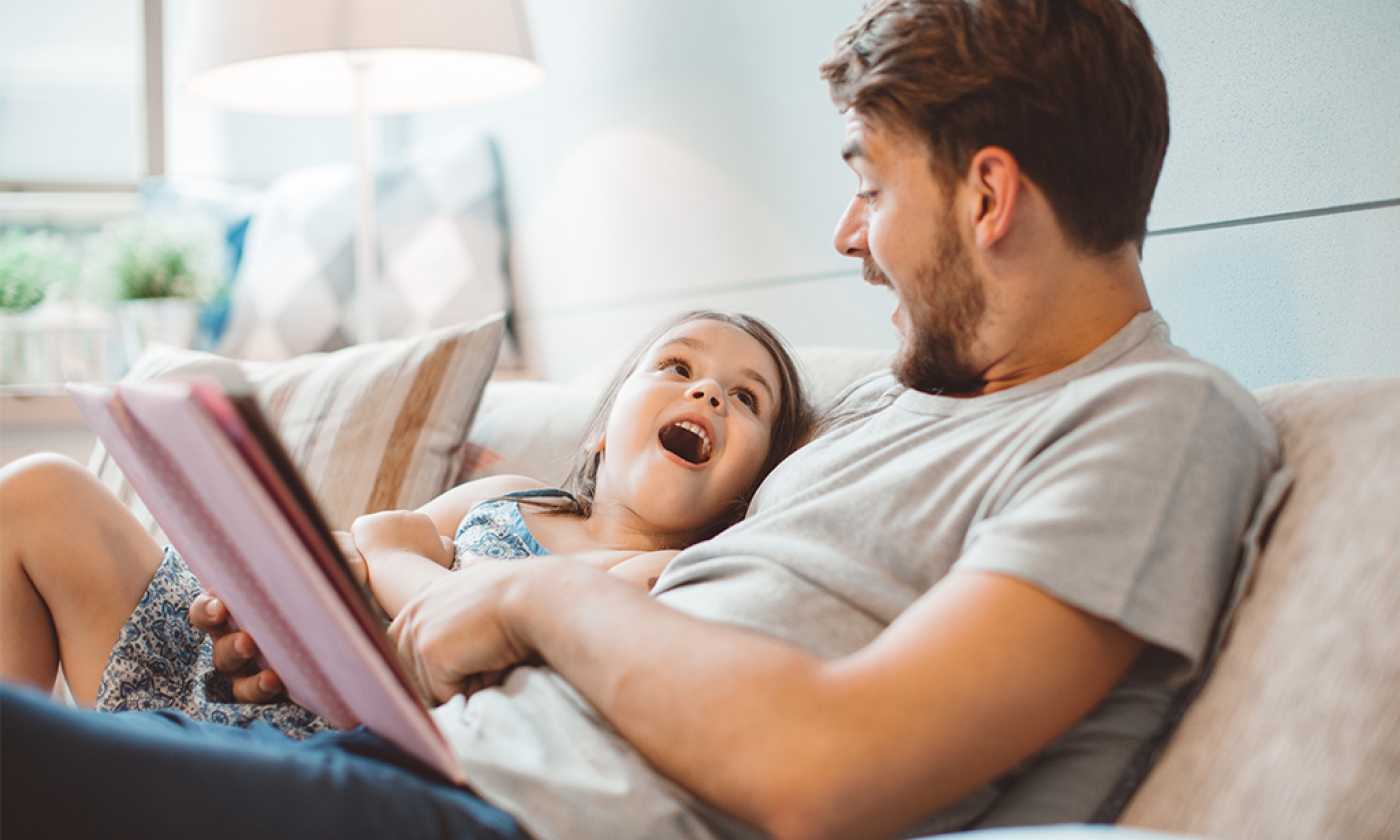 adult male and female child sitting on a couch reading a book