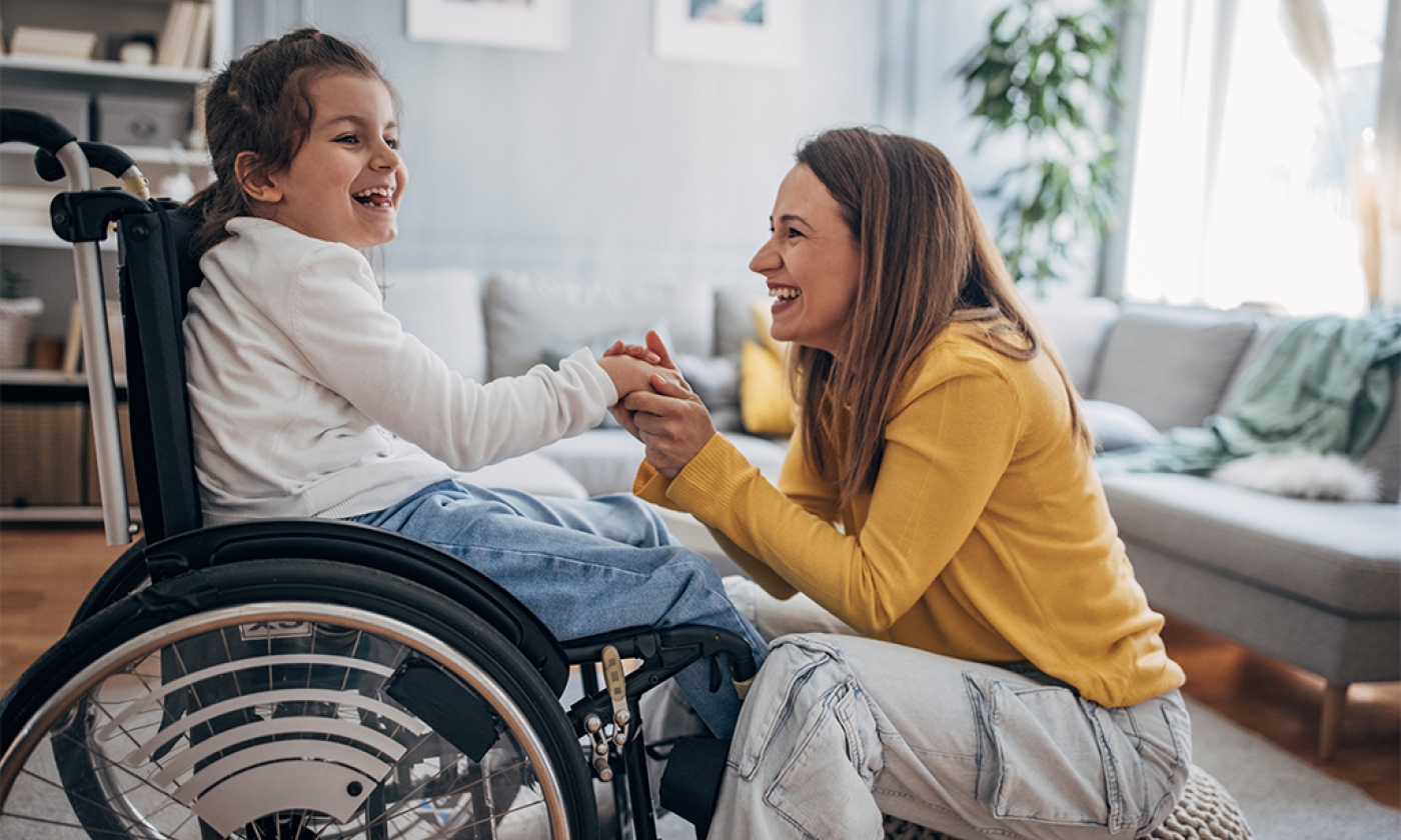 young female child in a wheelchair laughing holding hands with an adult female sitting in front of her
