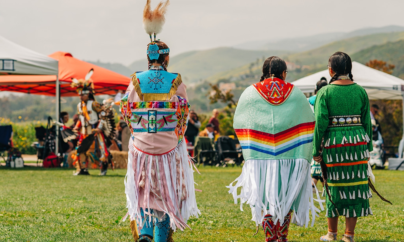 Three women dressed in Tribal attire walking together with their backs facing the camera.
